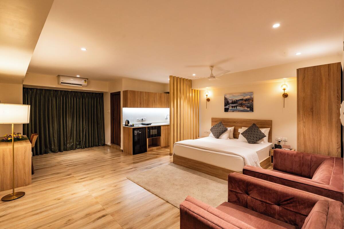 A modern hotel room with a bed, a desk, a chair, a sofa, and a painting on the wall.