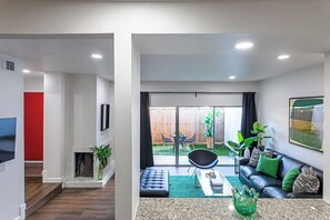 A modern living room with a fireplace, a black leather sofa, and a dining area with a glass table. - 3BR The Montrose Collective F! Steps to Food & Fun (Houston)