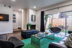 Ein modernes Wohnzimmer mit Kamin, einem an der Wand montierten Fernseher und einer Glastür, die auf eine Terrasse führt.