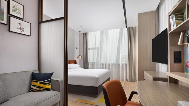 A hotel room with a bed, a desk, a chair, a television, and framed pictures on the wall. - Home2 Suites By Hilton Beijing Shunyi  (Shunyi)
