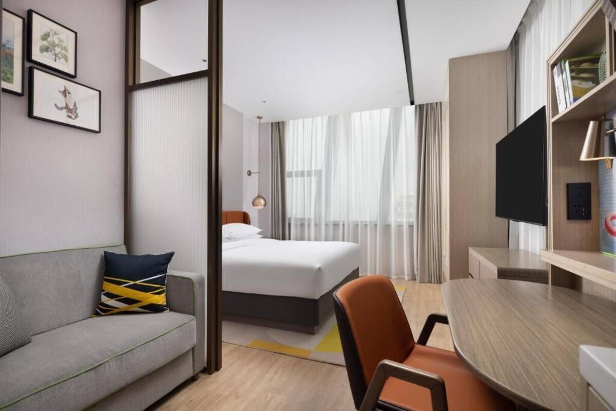 Habitación de hotel con cama, escritorio, silla, televisor y cuadros en la pared.