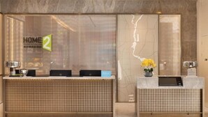 A hotel reception area with a reception desk, a digital check-in station, and a large window displaying the hotel's name. - Home2 Suites By Hilton Beijing Shunyi  (Shunyi)