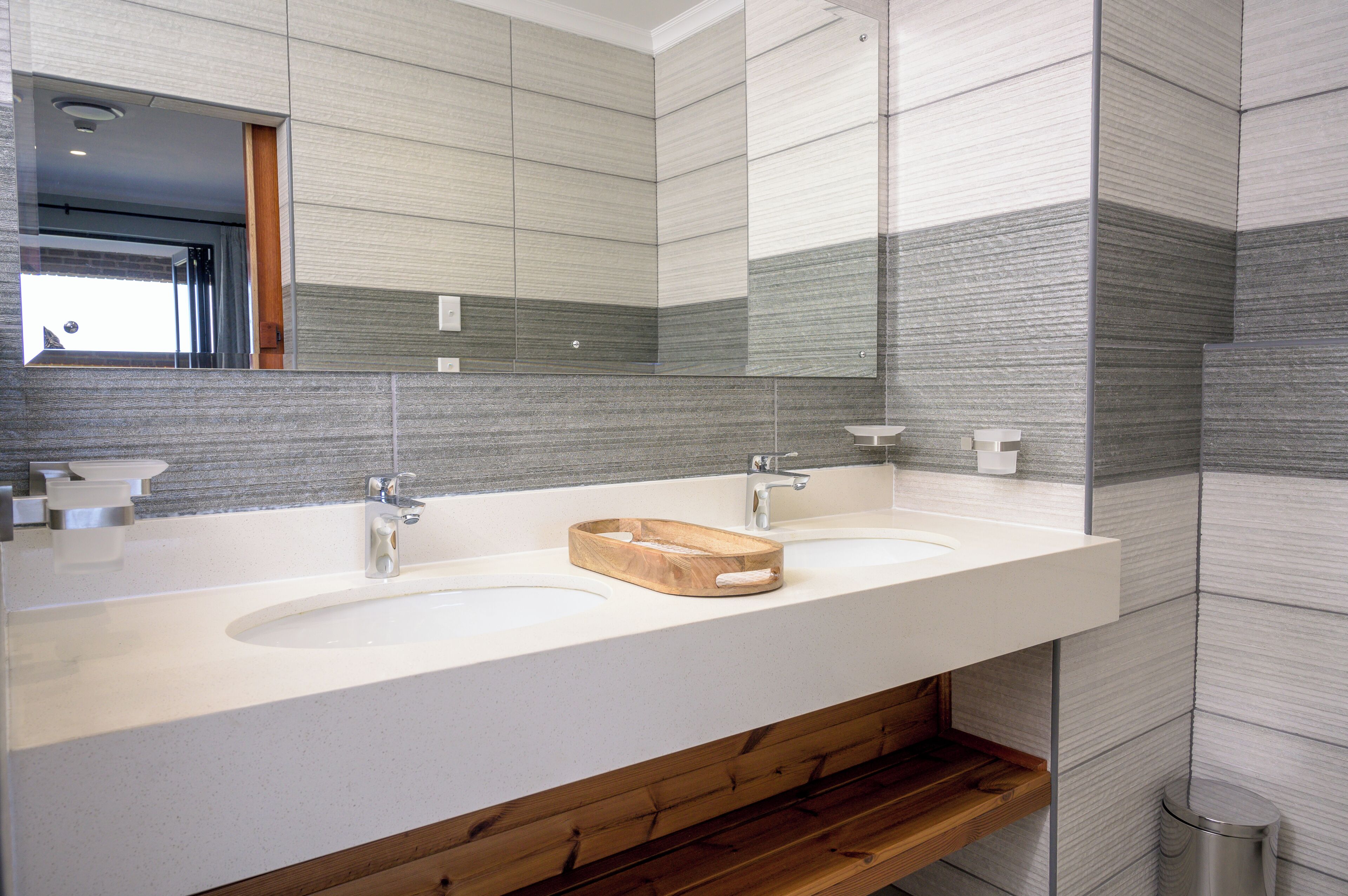 A modern bathroom with two sinks, a wooden vanity, and a large mirror.