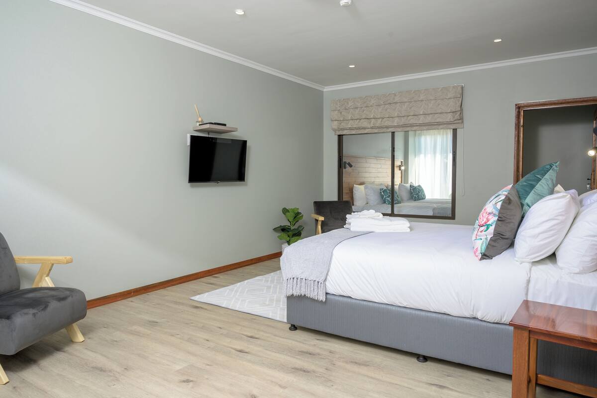 A modern bedroom with a bed, a TV, a mirror, and a chair.