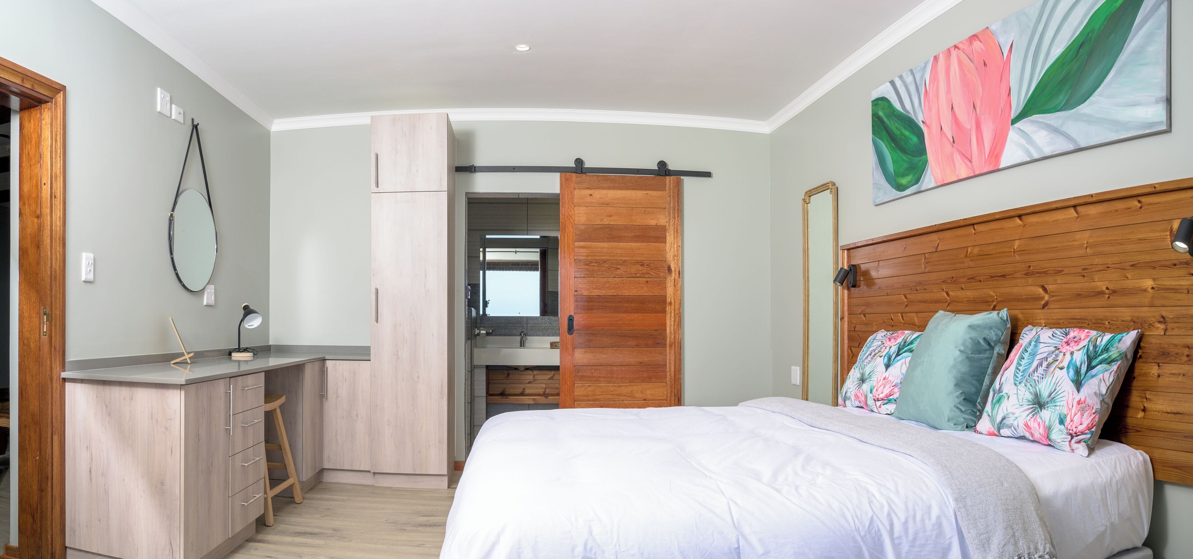 A bedroom with a bed, a wooden headboard, a desk, and a bathroom visible through an open door.