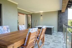 Un espace repas avec une table et des chaises en bois, un petit coin cuisine et un balcon doté d’une balustrade.