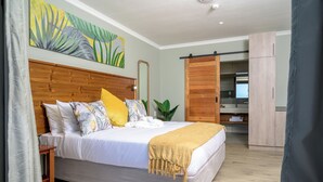 Una camera da letto con un letto grande, una testiera in legno, un comodino, uno specchio ampio e una porta scorrevole che dà su un bagno, con un quadro appeso al muro.