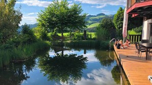 A wooden deck with a view of a pond, surrounded by greenery and hills. - Room-charming Guest Room in Ebbs Austria (Ebbs)