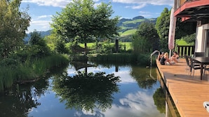A tranquil outdoor area with a wooden deck, a pond, and a view of rolling hills. - Room-charming Guest Room in Ebbs Austria (Ebbs)