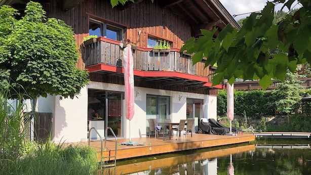 A two-story wooden house with a balcony, a wooden deck, and a pond in front. - Room-charming Guest Room in Ebbs Austria (Ebbs)