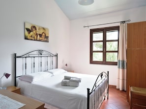 Ein Schlafzimmer mit Bett, Schreibtisch, Stuhl, einem Fenster mit Vorhängen und einem Gemälde an der Wand.