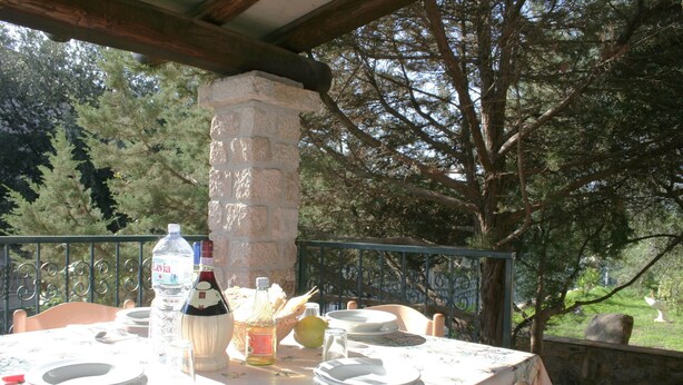 Un espacio al aire libre para comer con un pilar de piedra, una mesa puesta con platos, cubiertos y una botella de agua.