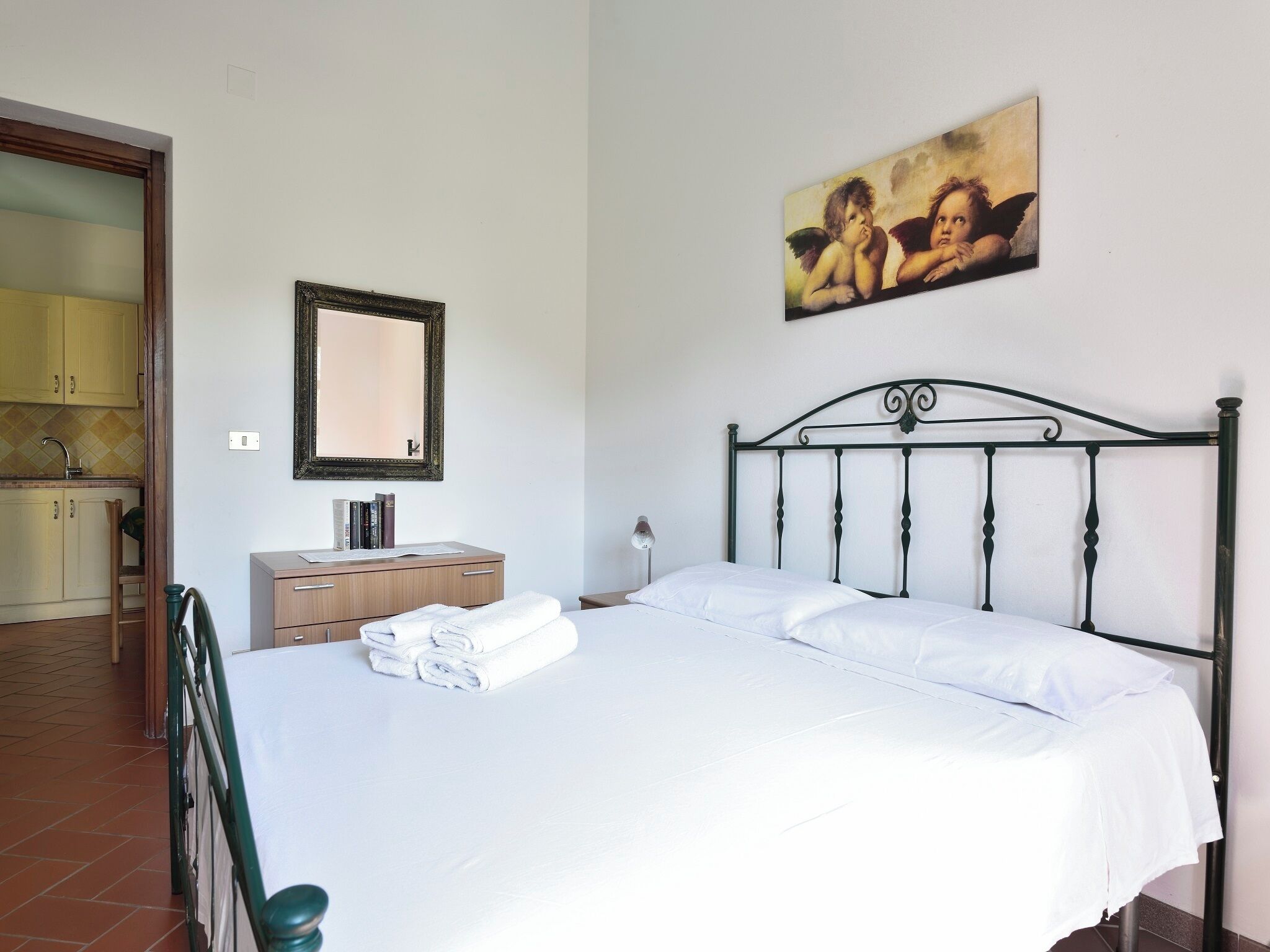 A bedroom with a bed, a dresser, a mirror, and a painting on the wall.