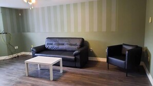 Olohuoneessa on tumma nahkasohva, samanvärinen nojatuoli ja pieni valkoinen pöytä.