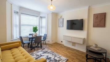 A living room with a sofa, dining table, chairs, a TV, and artwork on the walls.