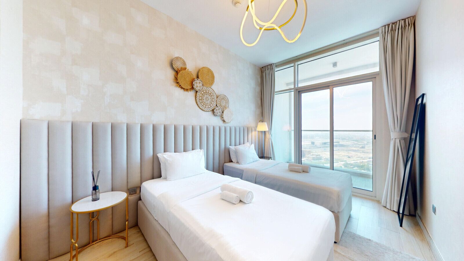 A hotel room with a large bed, a smaller bed, a bedside table, a lamp, and a view of the city through large windows.