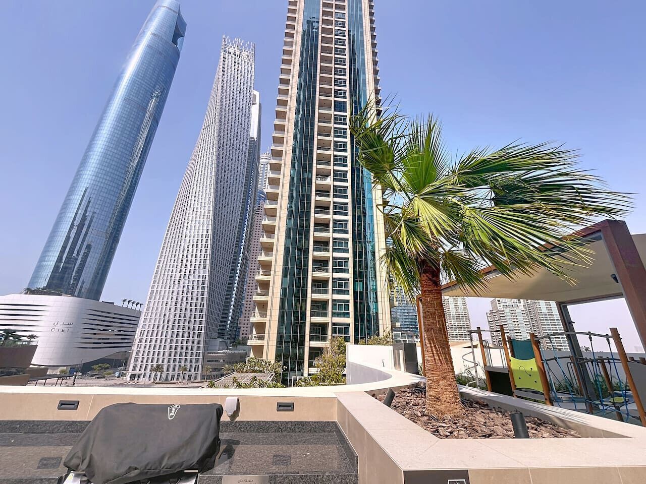 Ein modernes Hochhaus mit Glasfassade, umgeben von Palmen und einem Spielplatz.