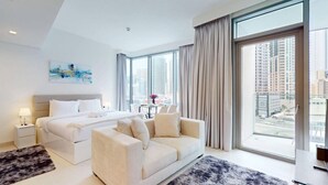 Una camera d'hotel moderna con un letto grande, una poltrona, un tavolo da pranzo e vista sulla città attraverso ampie finestre.