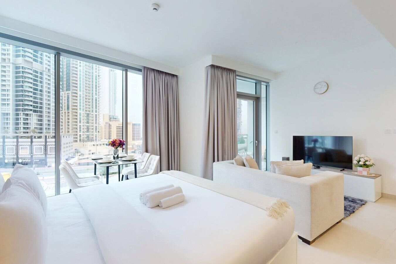 Habitación de hotel con una cama grande, un sofá, televisión y un balcón con mesa y sillas.