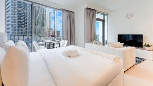 Una camera d'albergo con un letto, un divano, una televisione, un tavolo da pranzo con sedie e vista su alti edifici.