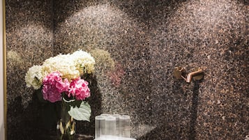 A wall-mounted clock with a leaf design, a mirror reflecting a vase with flowers, and a metallic door handle.