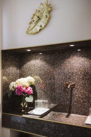 A wall-mounted clock with a leaf design, a mirror reflecting a vase with flowers, and a metallic door handle. - Hotel AVKA Vienna (Vienna)