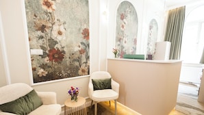 A reception area with a floral mural, two armchairs, a small table with a vase, and a reception desk.