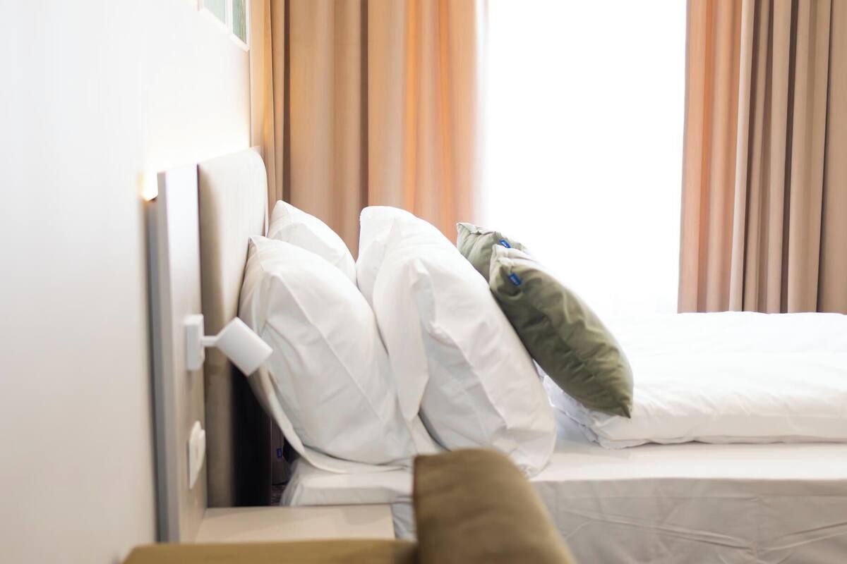 Une chambre d’hôtel avec un lit, une fenêtre avec des rideaux et un canapé marron.