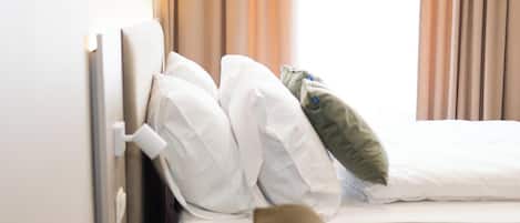 A hotel room with a bed, a window with curtains, and a brown sofa.