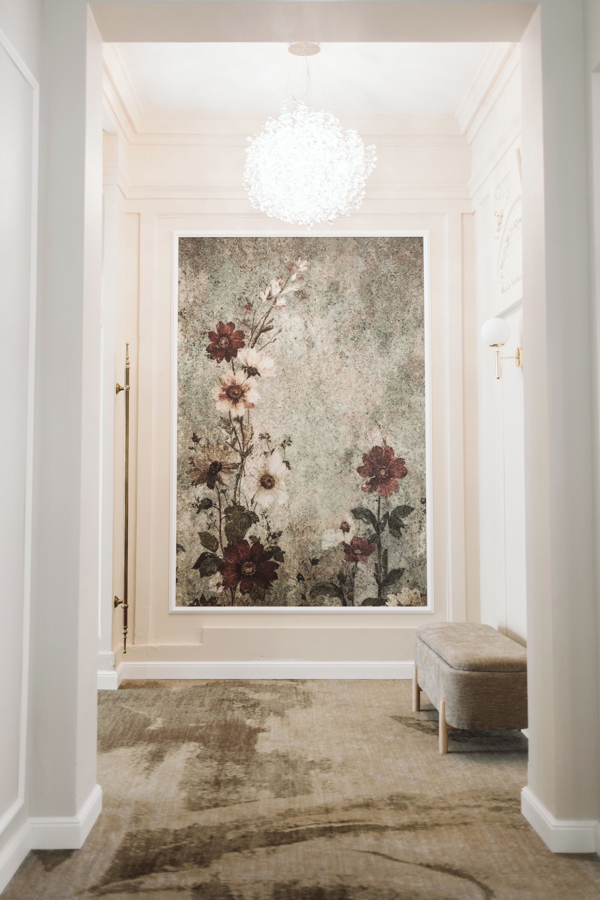 Un pasillo con un cuadro grande de flores en la pared, un banco y una araña.