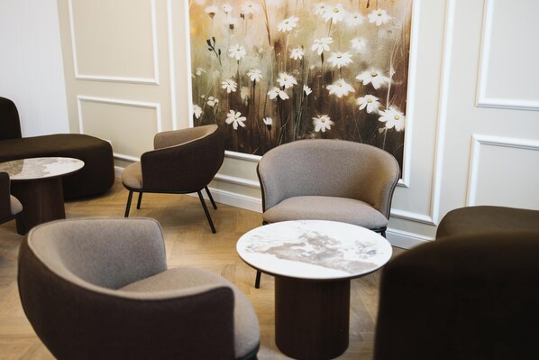 Ein modernes Interieur mit runden Tischen und grau gepolsterten Stühlen, einem floralen Wandbild und Holzboden.