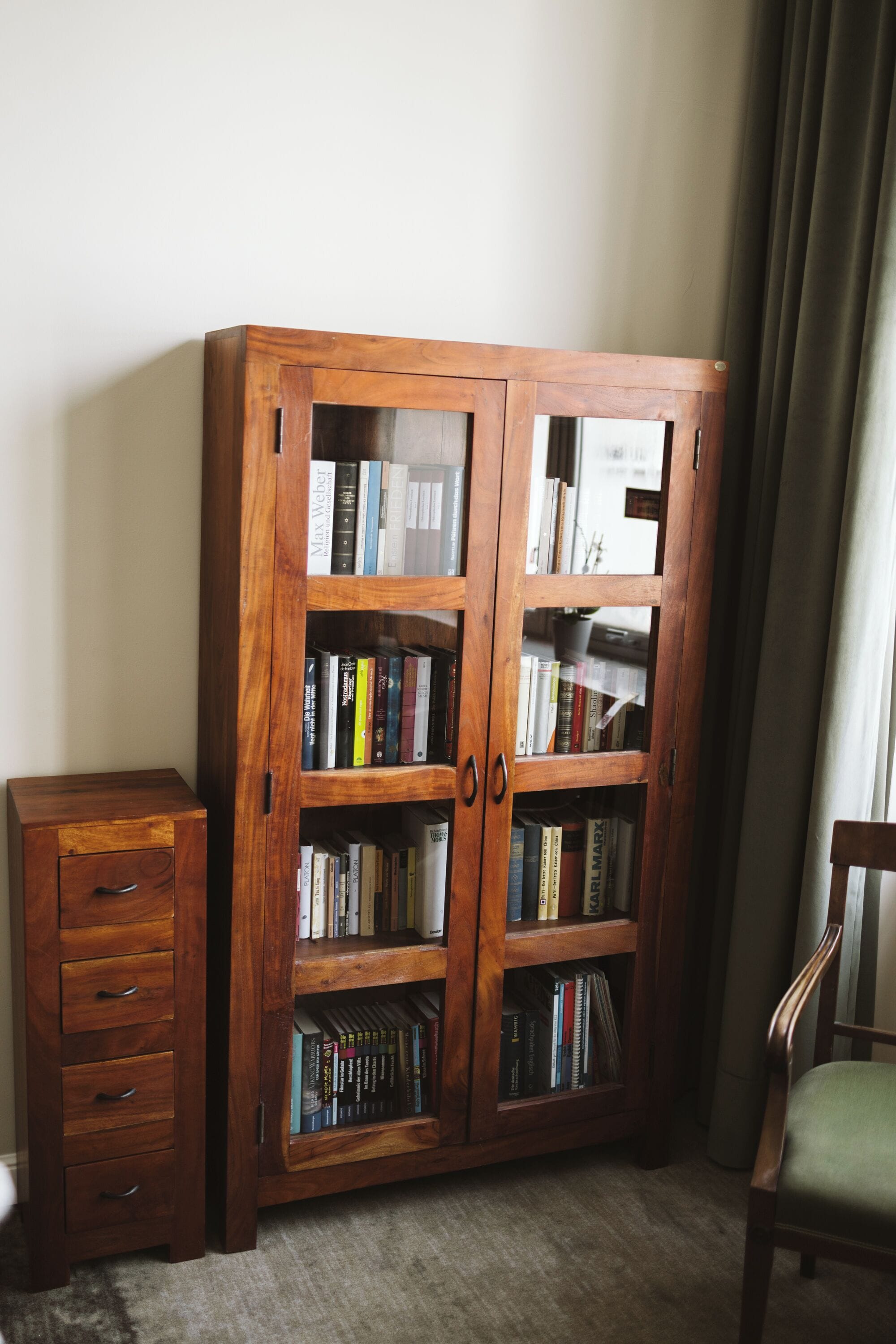 A wooden bookcase with multiple shelves, a small wooden cabinet with drawers, and a green upholstered chair.