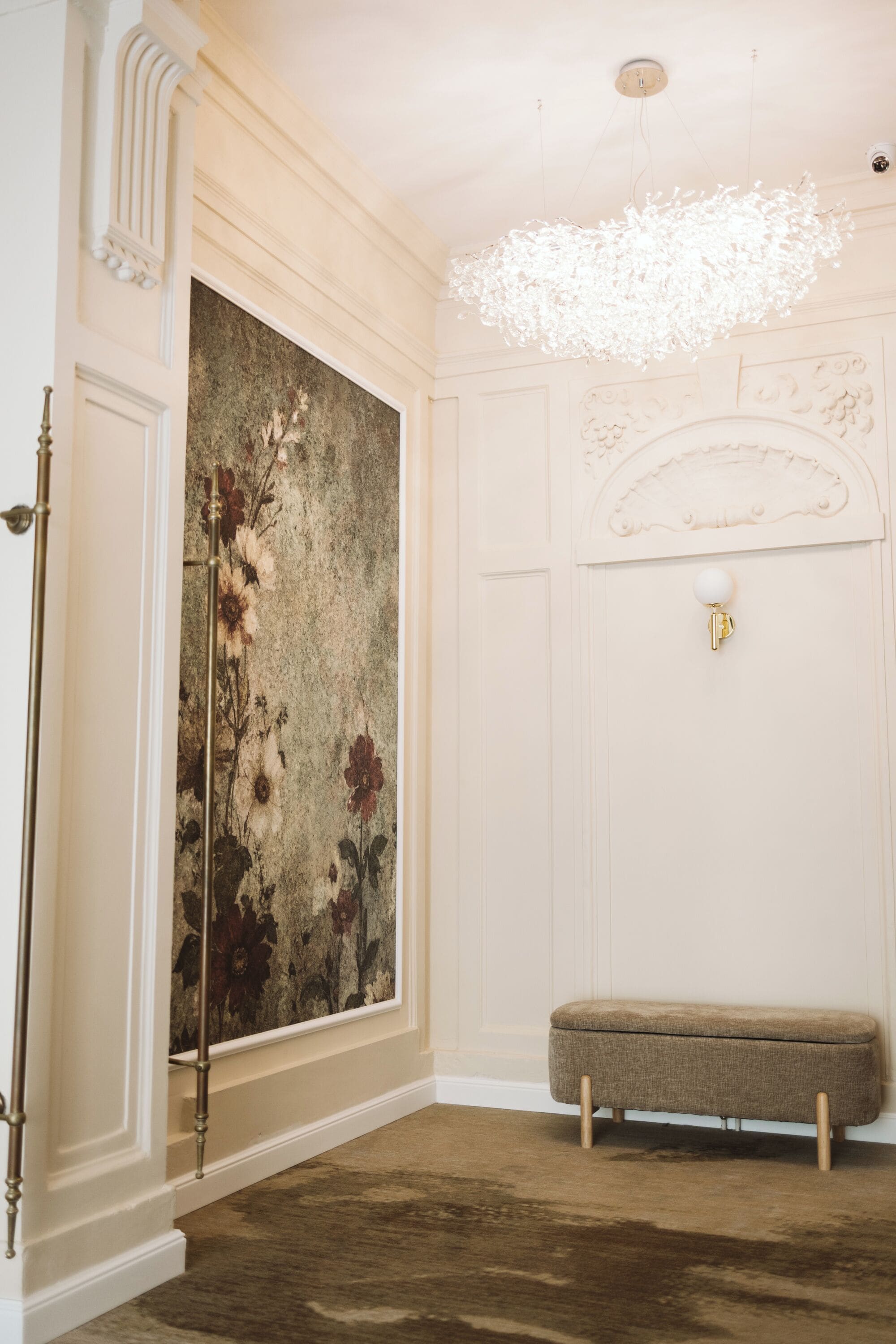 Um quarto com um grande quadro floral na parede, um banco e um lustre.