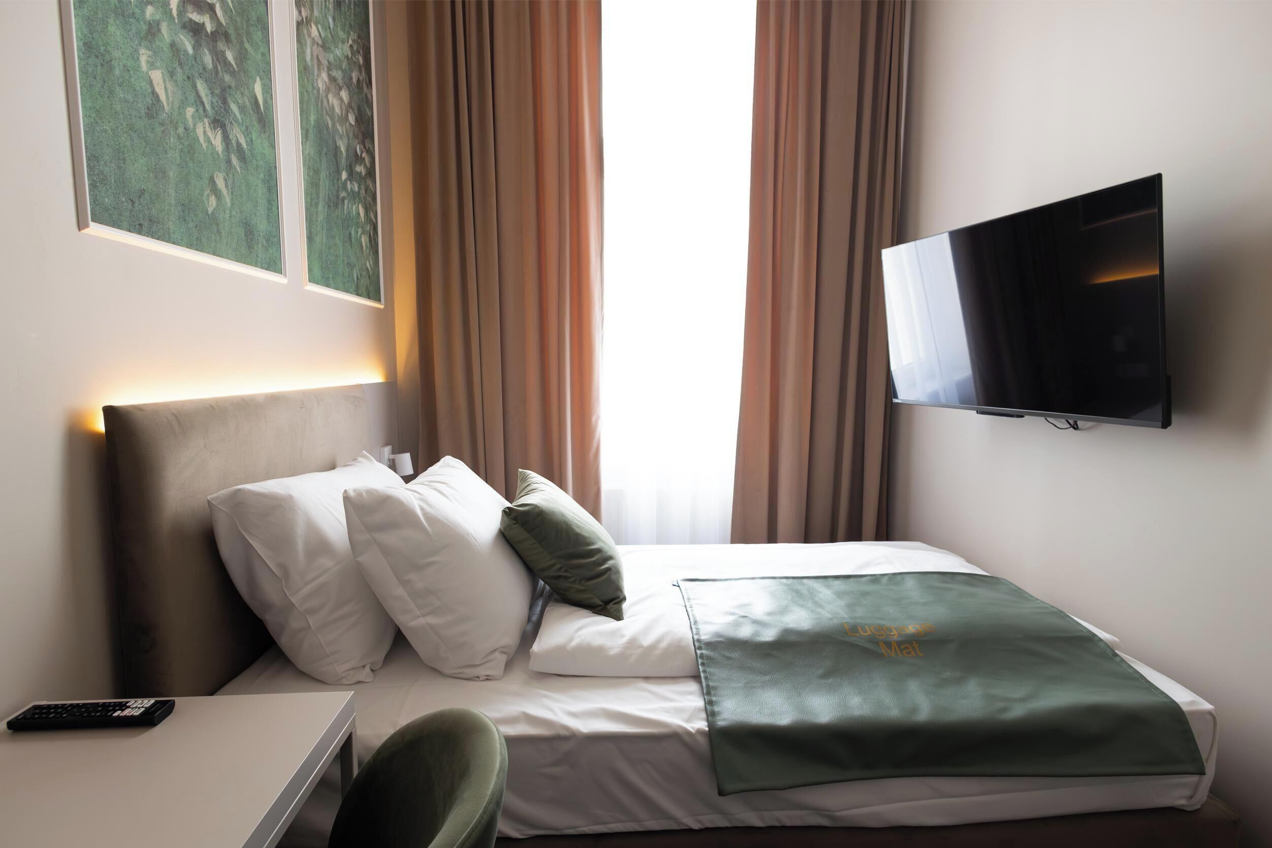 A hotel room with a bed, a TV mounted on the wall, a bedside table with a remote control, and a chair.