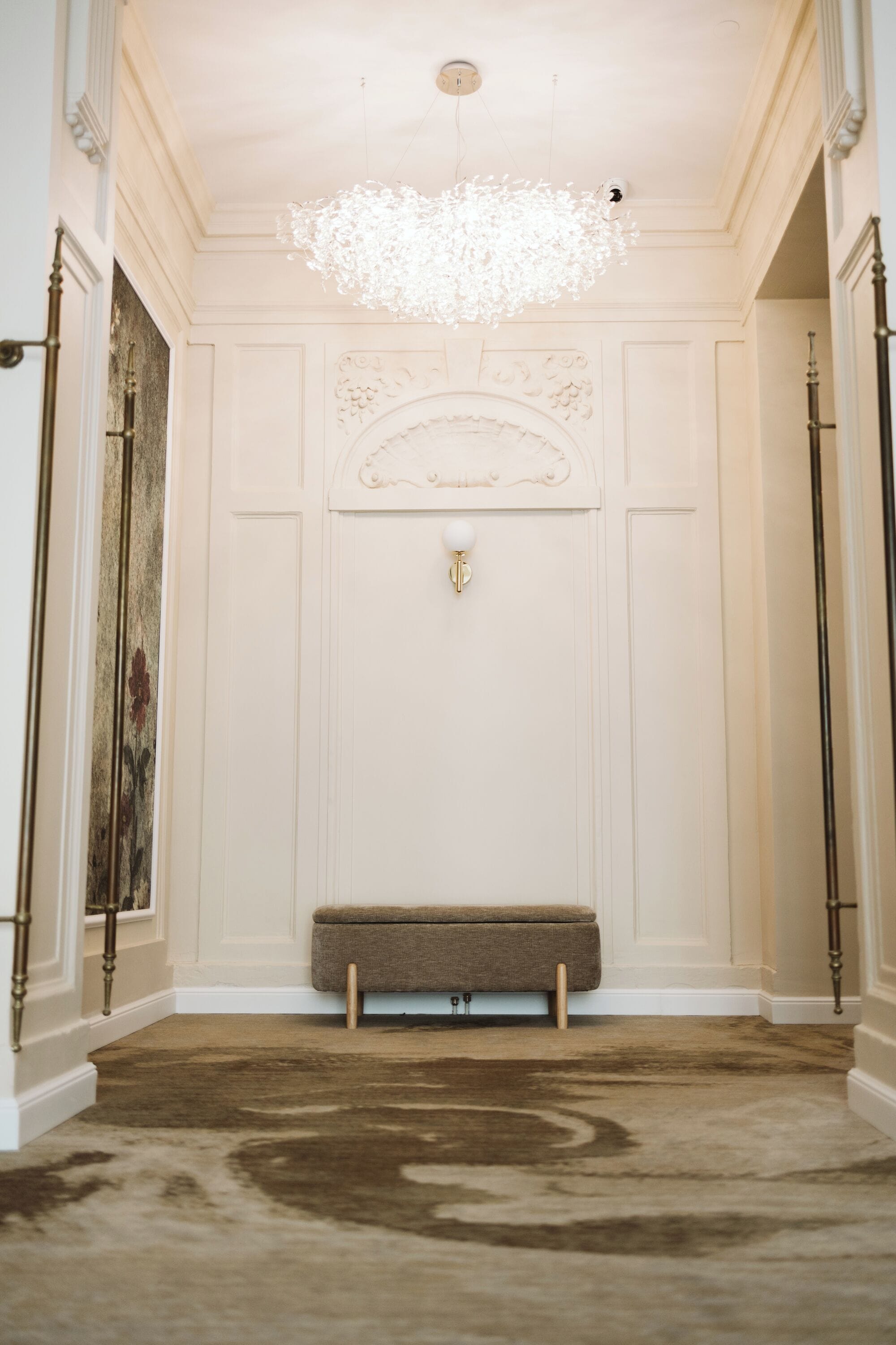 A hallway with a bench, a chandelier, and a door with a decorative panel.