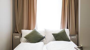 A bed with white linens and two pillows, a nightstand with a power outlet, and beige curtains.