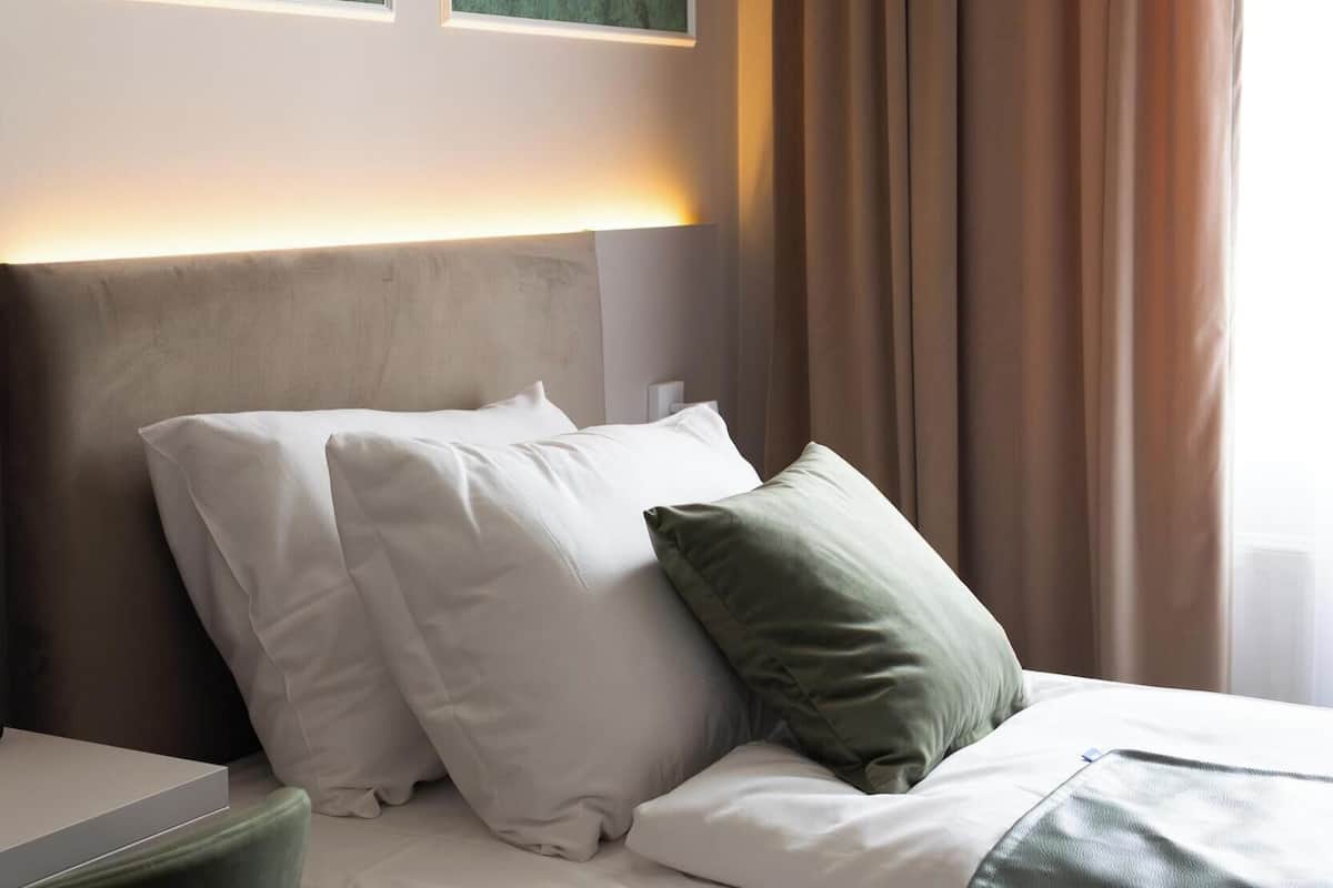 Un lit bien fait, avec des oreillers blancs et verts, un plaid vert et une tête de lit dotée d’un panneau lumineux.