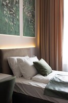 Un letto rifatto con cuscini bianchi e verdi, una coperta a maglia verde e una testiera con pannello illuminato.
