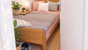 Une chambre à coucher avec un lit en bois, des tables de chevet, une petite table, une lampe, une plante en pot et une paire de chaussures.