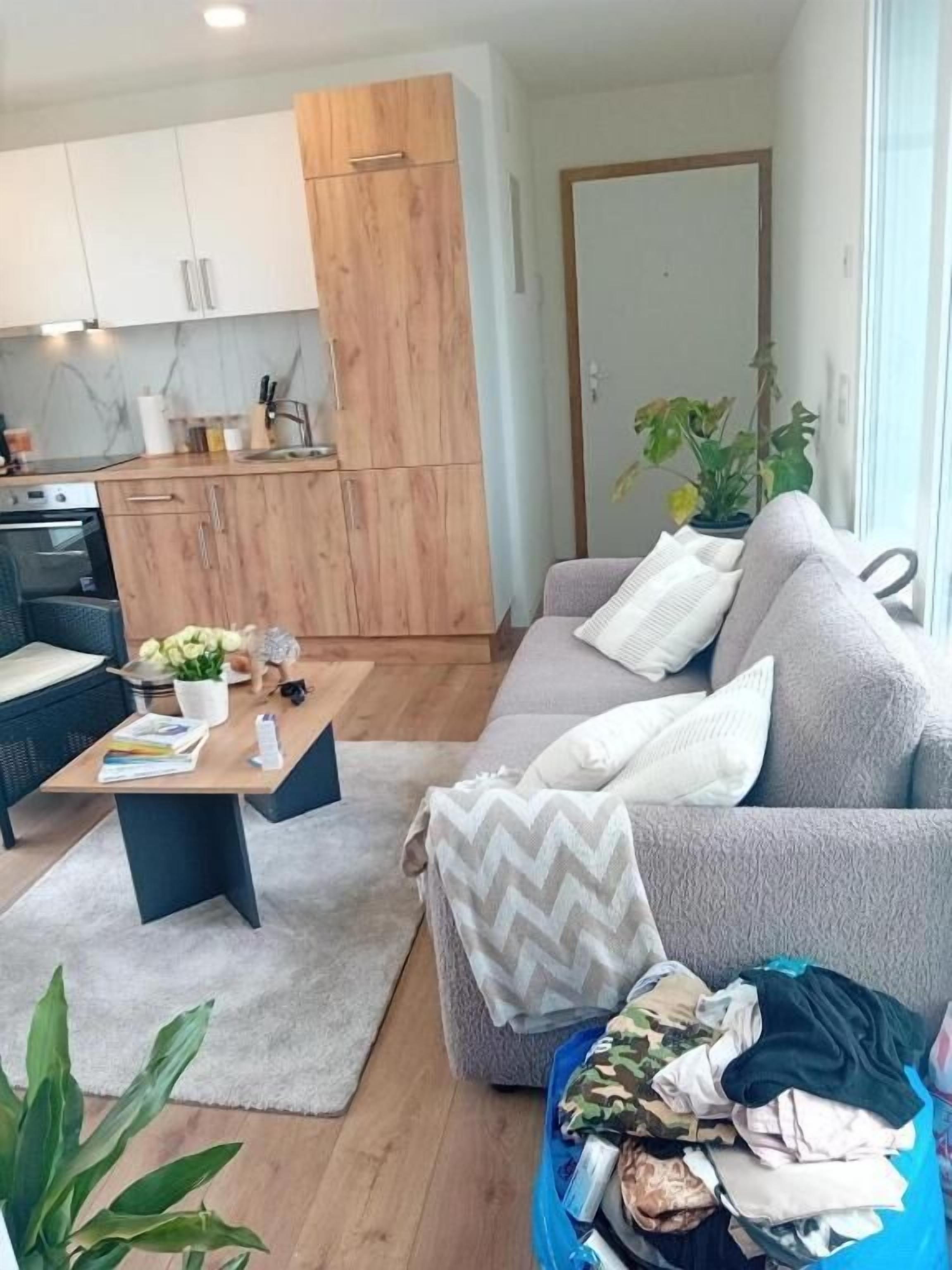 Una sala de estar con un sofá, una mesa de centro y una pila de ropa en el suelo.
