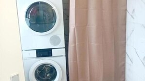 Une petite salle de bain équipée d’un lave-linge, de toilettes et d’un rideau de douche.