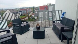Un balcon agrémenté de meubles en osier, d’une petite table et offrant une vue sur les bâtiments et la verdure.
