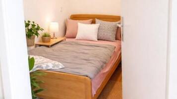 Une chambre à coucher avec un lit en bois, une table de chevet avec une lampe, une étagère fixée au mur et une porte donnant sur une autre pièce.