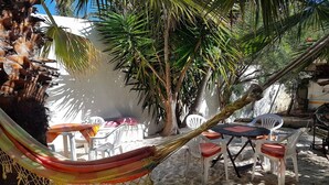 Eine Hängematte, Sitzgelegenheiten im Freien und ein Tisch in einem sonnigen, sandigen Außenbereich.