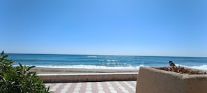 Blick auf einen Strand mit blauem Himmel, sandigem Ufer und einem gepflasterten Weg.