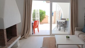 Een woonkamer met een bank, een salontafel, een open haard en een glazen schuifdeur die leidt naar een terras met een tafel en stoelen.