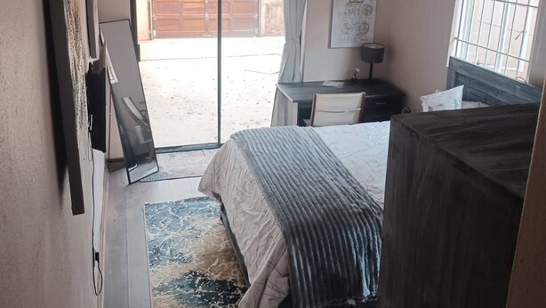 Un dormitorio con cama, escritorio, silla, ventana con rejas y vista al exterior.