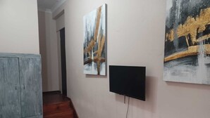 Una habitación con una cama, un armario gris, un televisor montado en la pared y dos cuadros.