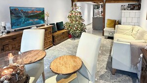 A modern living room with a large flat-screen TV, a wooden dining table, and a Christmas tree. - Elegant Lake Zurich House with Stunning Views and Private Terrace (Stäfa)