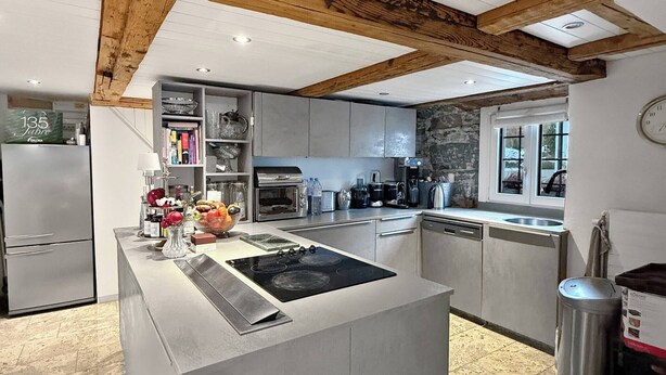 A modern kitchen with a central island, built-in appliances, and a stone accent wall. - Elegant Lake Zurich House with Stunning Views and Private Terrace (Stäfa)